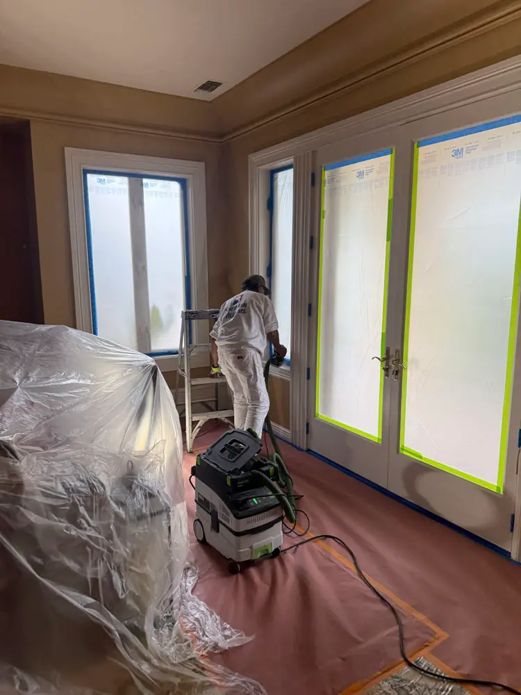 Piñon Painting crew member prepping and sanding trim beside fully masked French doors